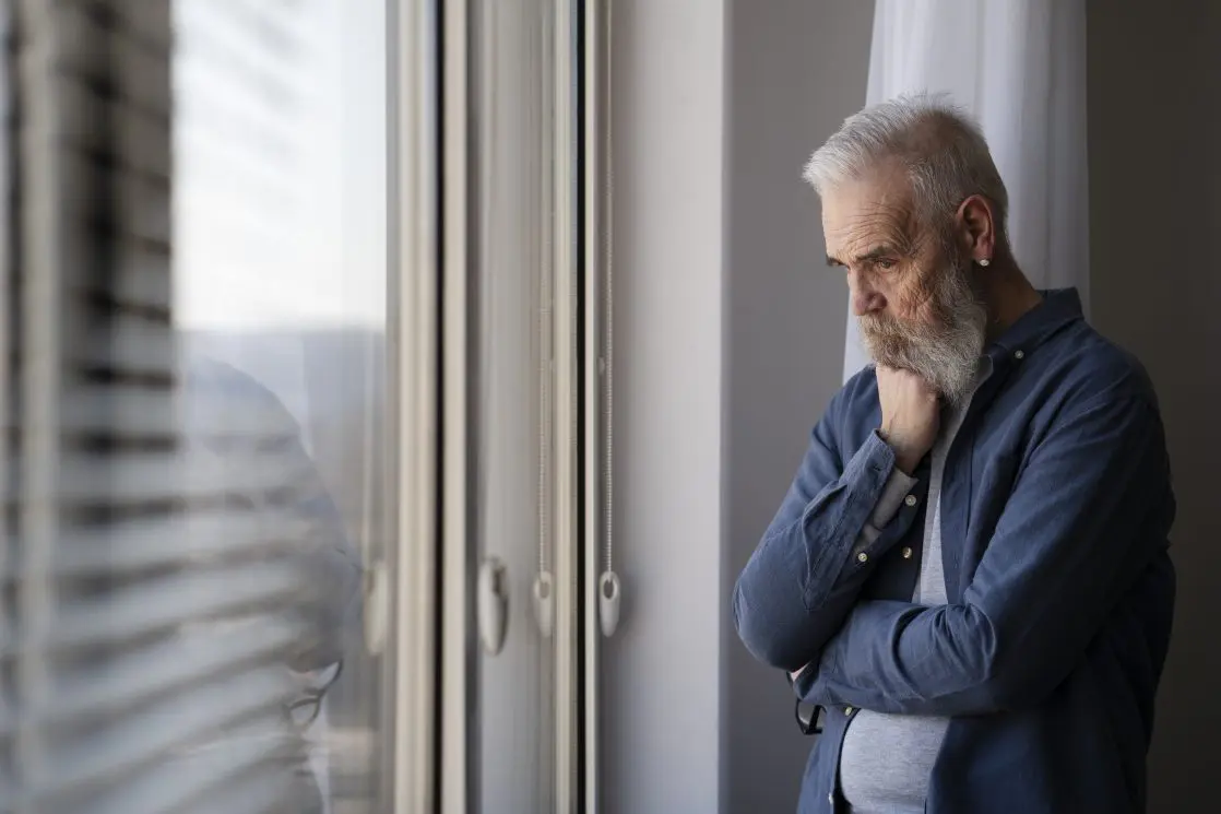 sad older man at home looking out window