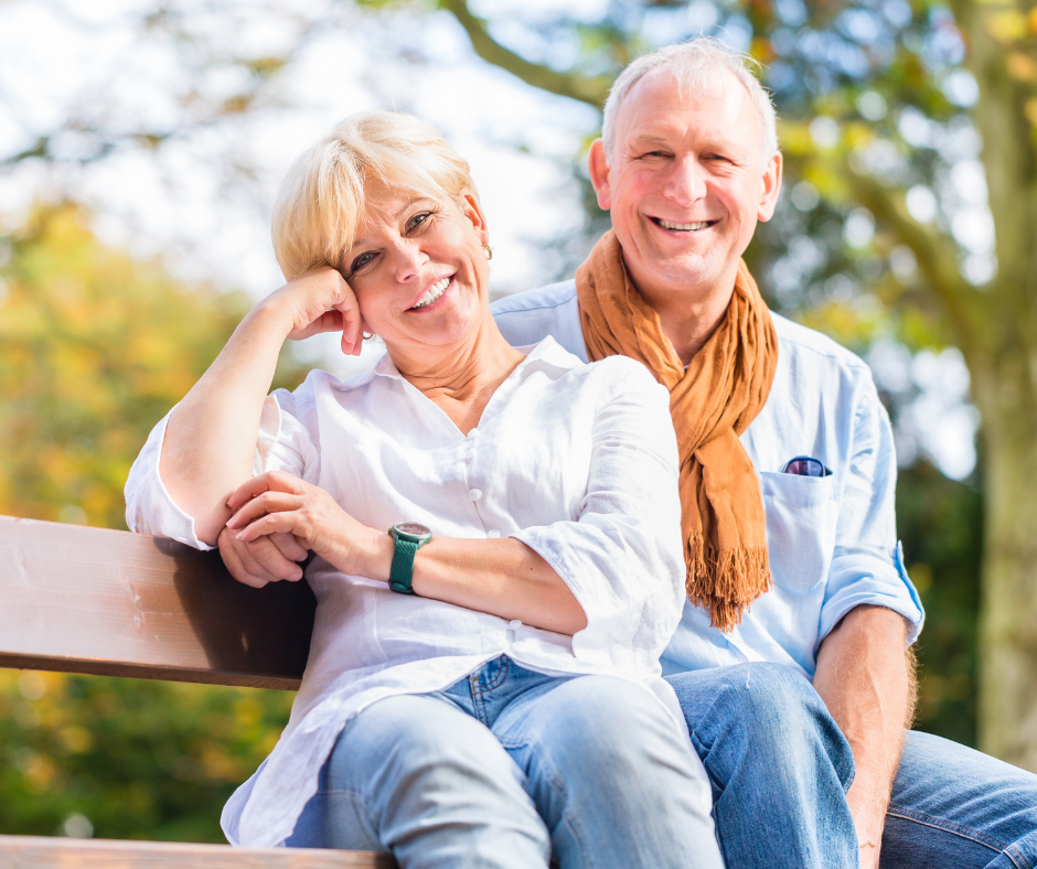 older couple smiling while sitting on a bench
