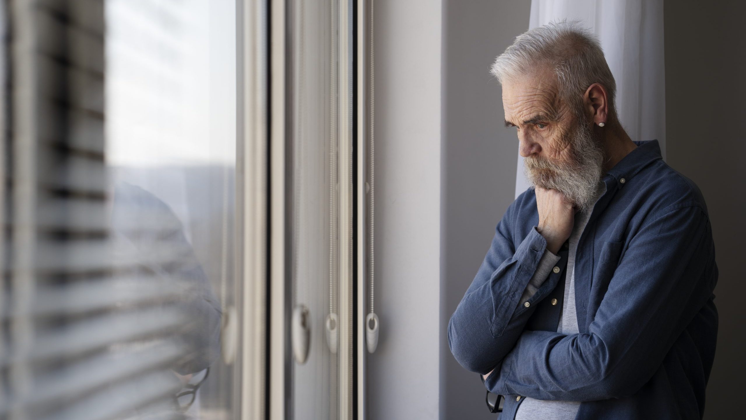 sad older man at home looking out window
