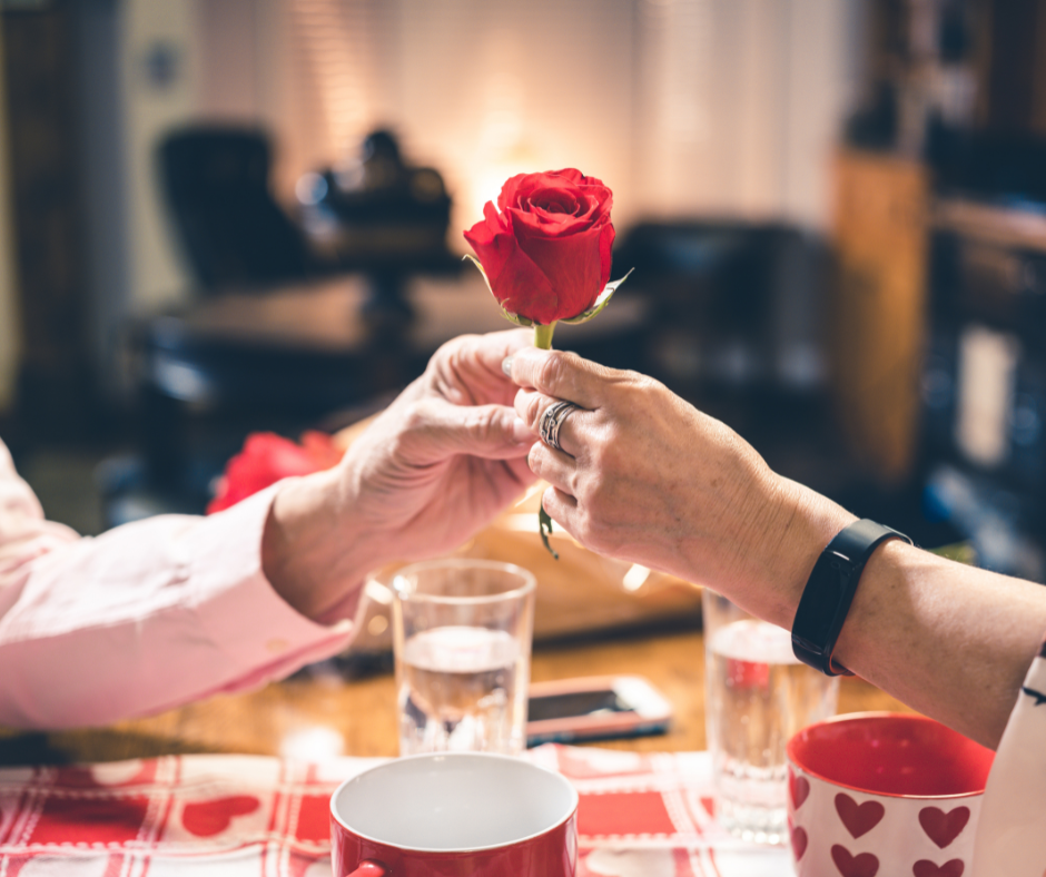 A woman's hand accepting a red rose from a man's hand over a dinner date.